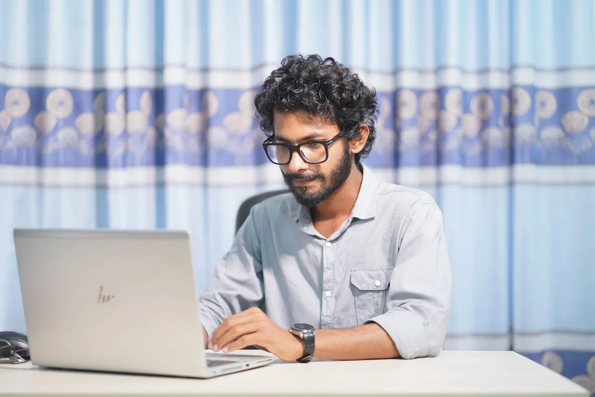 A web designer works on a client website layout on a laptop at a desk.