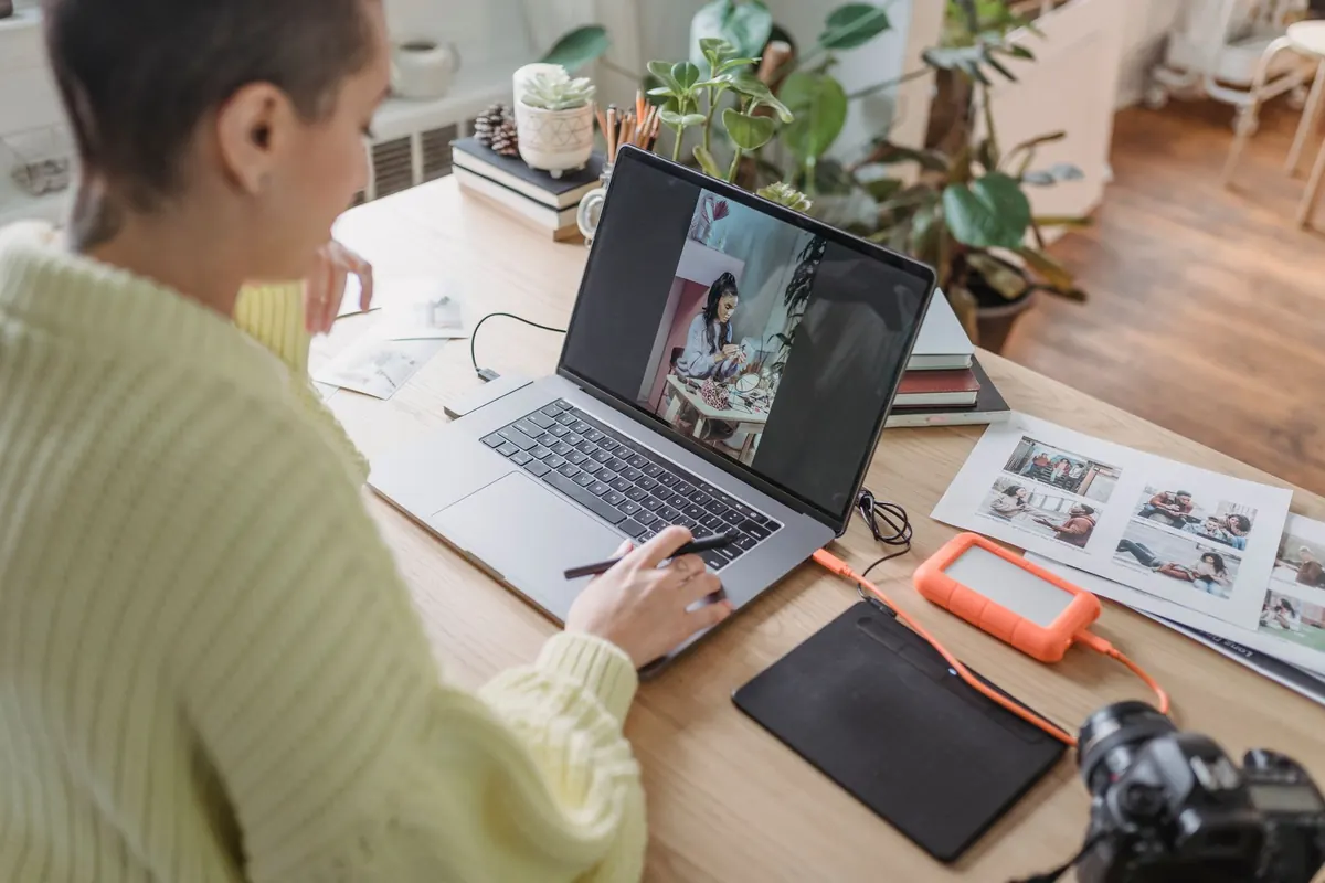 A photographer sits at a desk reviewing a set of portrait photos on a laptop screen.
