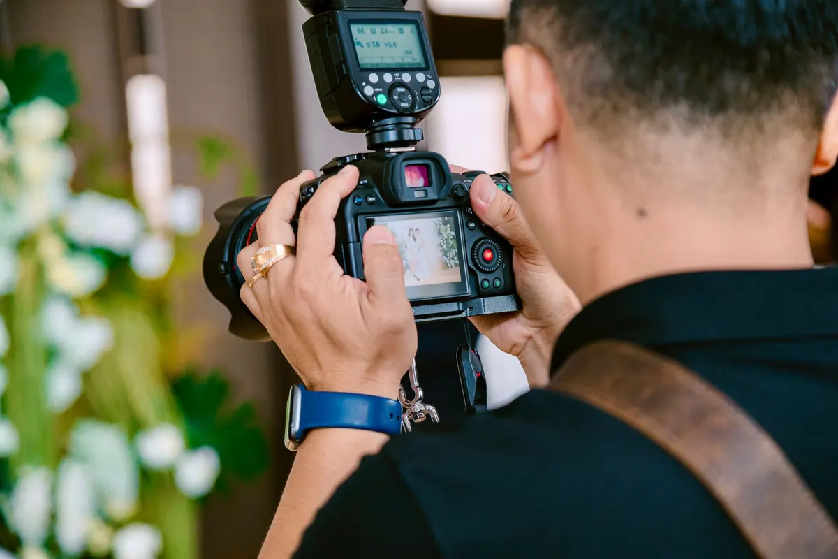 A wedding photographer holds a camera and checks a shot during an outdoor ceremony.