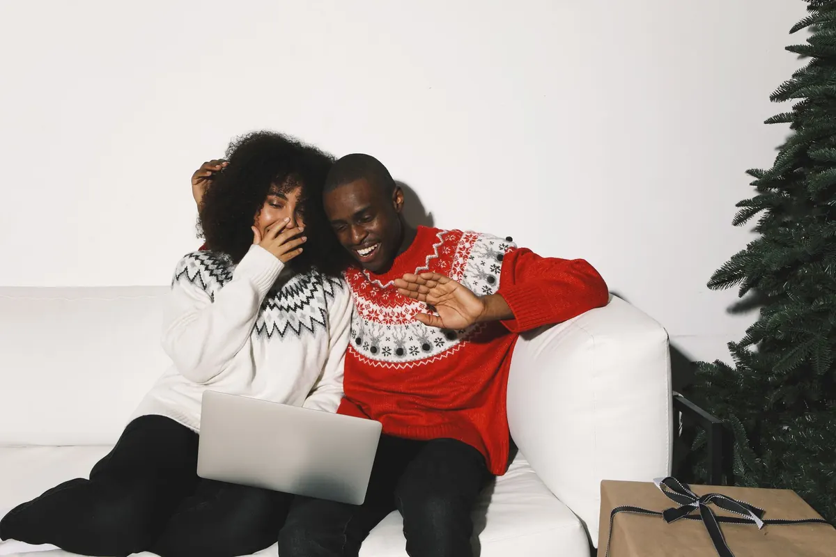 A couple sits on a sofa looking at travel plans together on a laptop.
