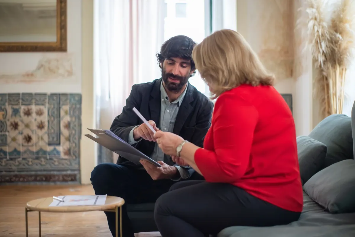 A consultant and a client talk over documents at a desk in a small, bright office.