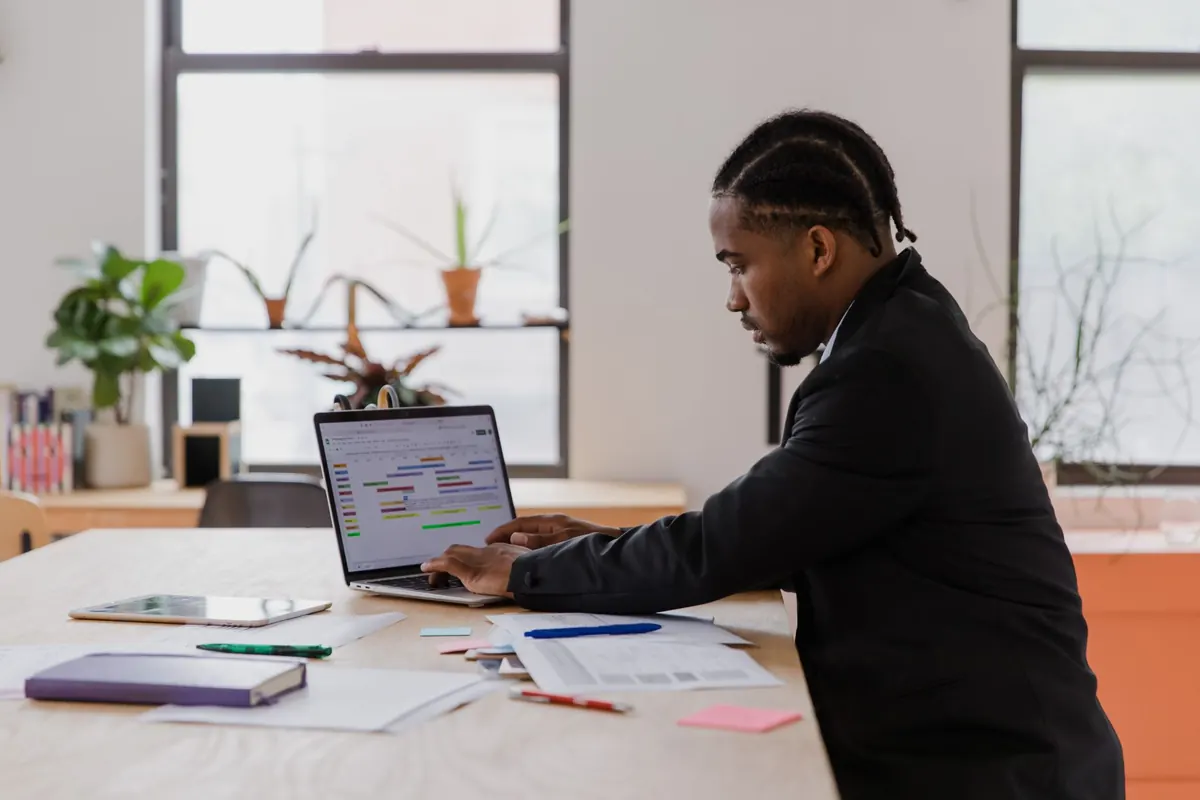 A small business owner checks a paper calendar beside an open laptop on a wooden table.