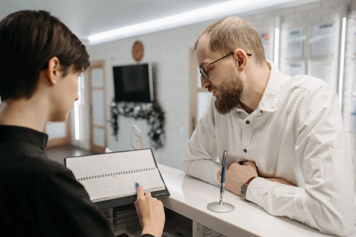 A receptionist at a small clinic front desk checks the appointment calendar on a computer screen.