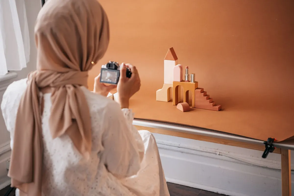 A woman photographing handmade products on a table near a window for her online shop.