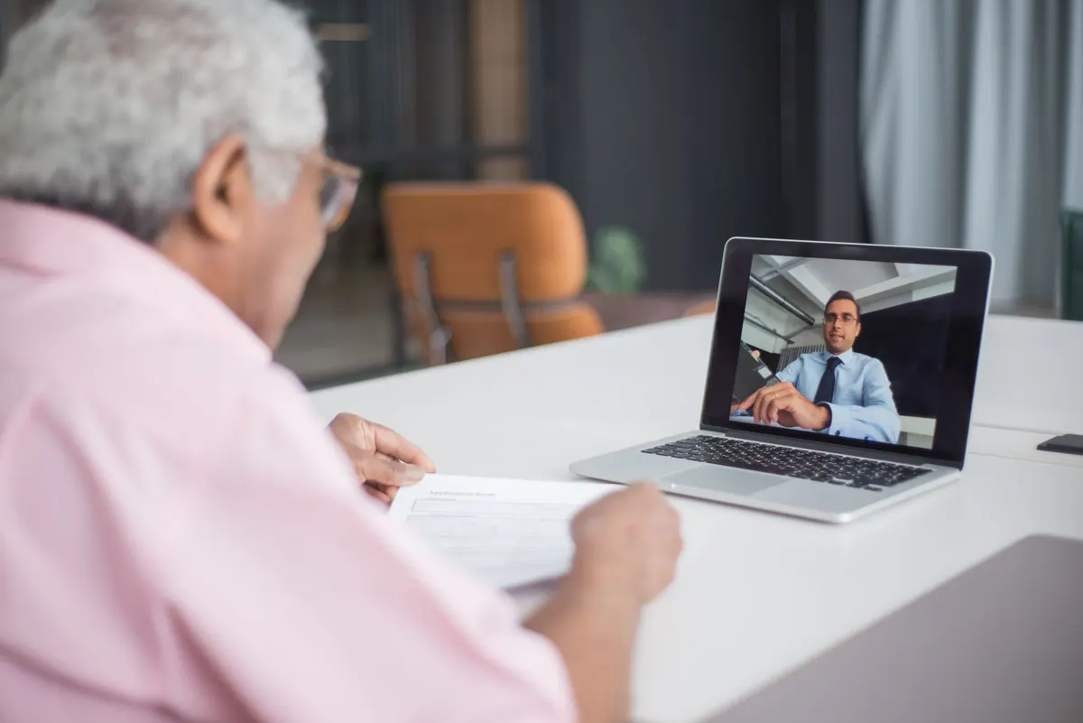 A consultant talking with a client on a video call while taking notes in a notebook.