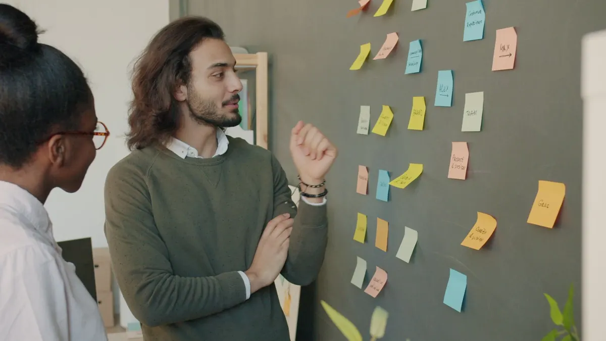 Two colleagues arranging sticky notes on a wall to plan how customers move from enquiry to sale.