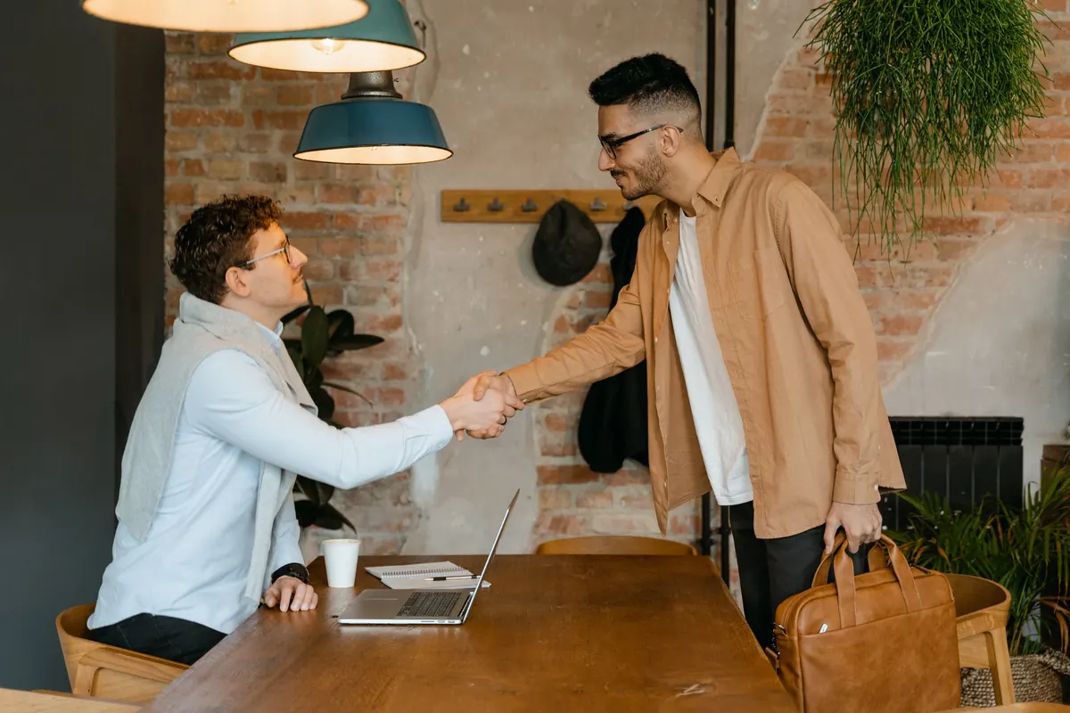 A designer showing a website on a laptop to a small business owner across a cafe table.