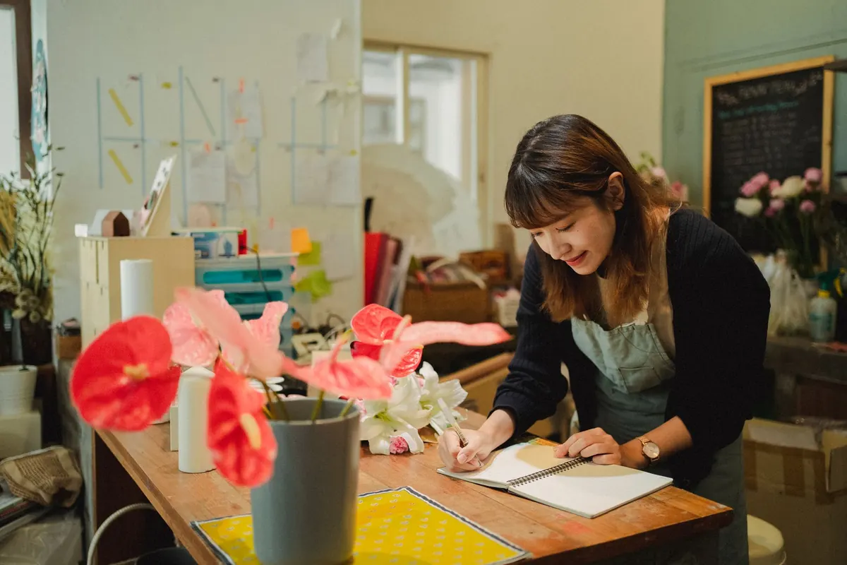 A florist standing among buckets of flowers, taking a customer order on the phone.