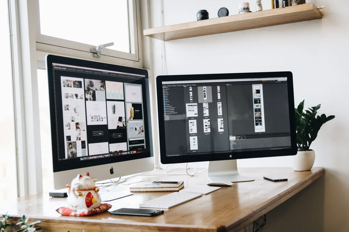 A web designer compares two website drafts side by side on a laptop and a second monitor.