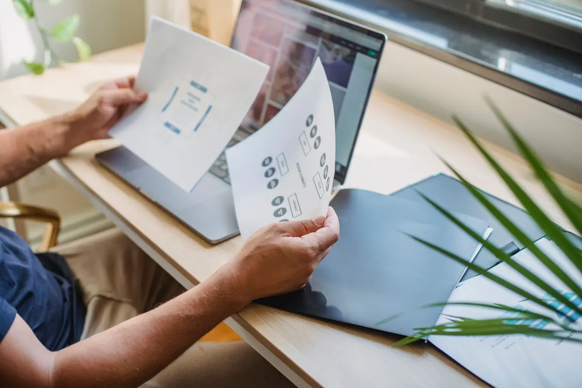 A designer at a desk comparing two website designs on a laptop and a large monitor.