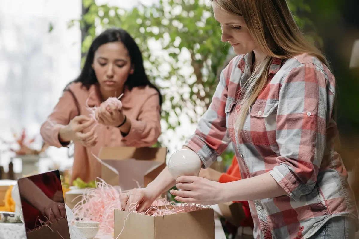 A florist wrapping flowers at a shop counter while checking an order list on a tablet.