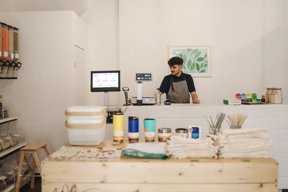 A shop owner sits at a counter with a laptop, working on a new website between customers.