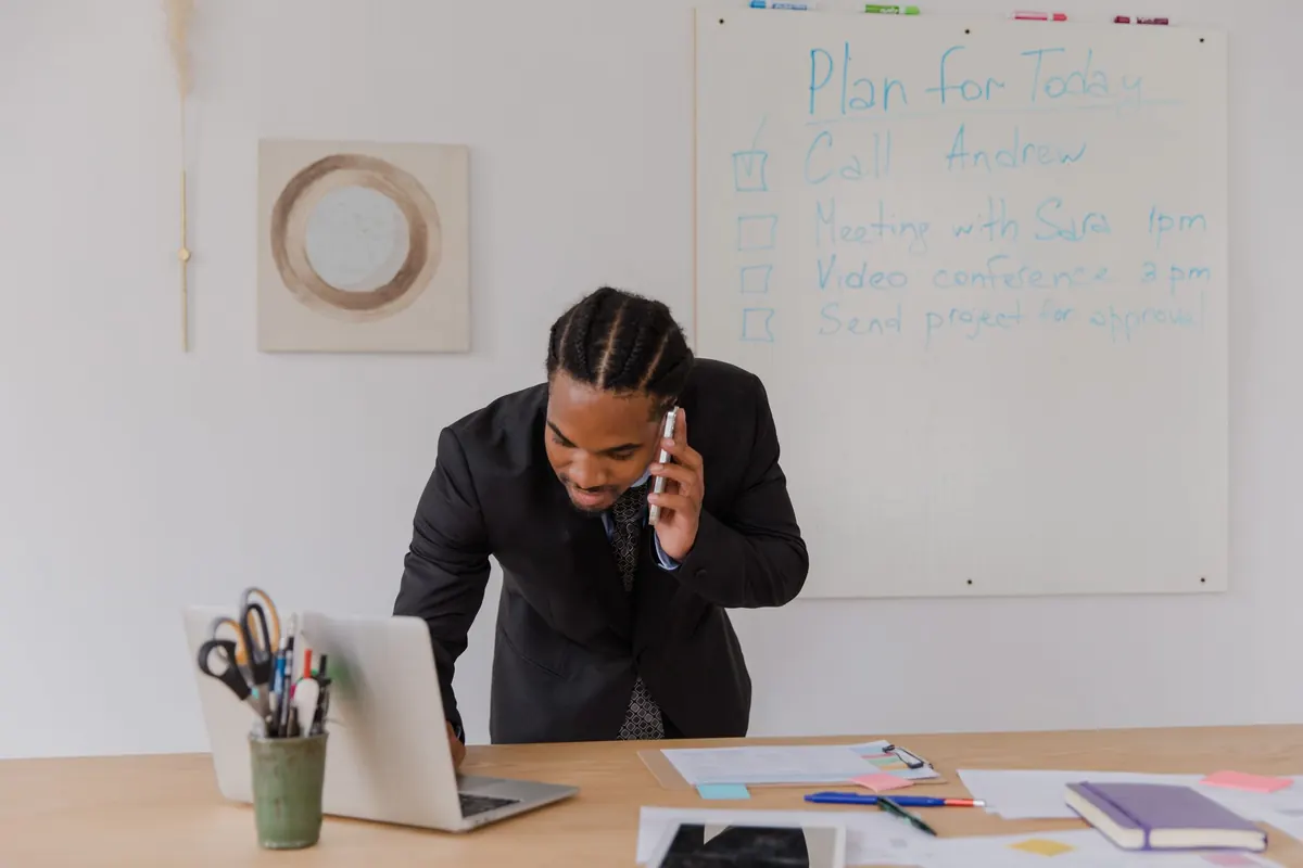 A small business owner on a phone call while looking at a laptop at home.