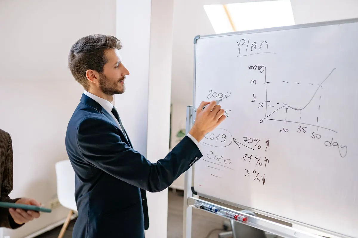 A marketer sketches the steps of a sales funnel on a whiteboard in a small office.