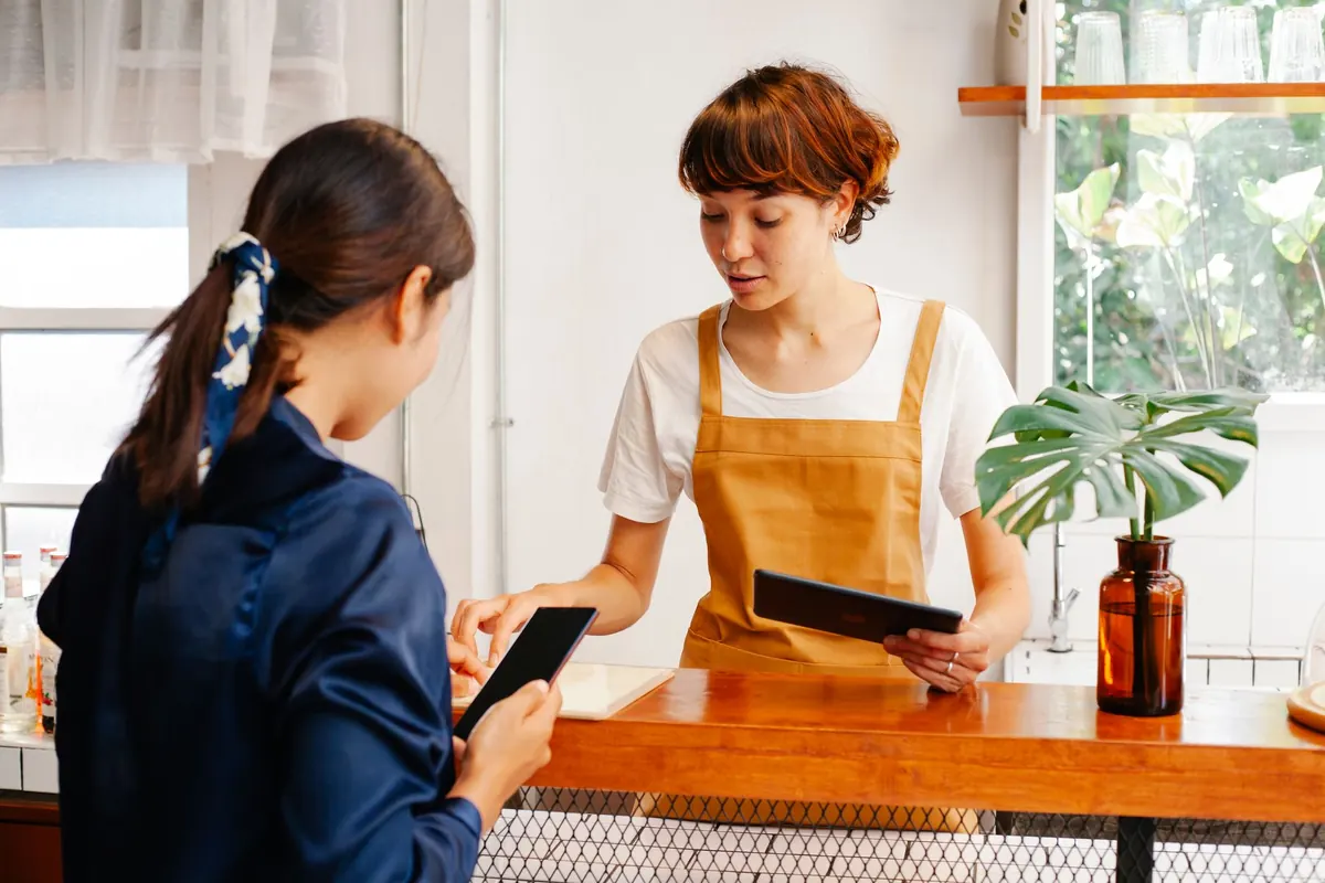 A small business owner checks new customer bookings on a tablet at the shop counter.