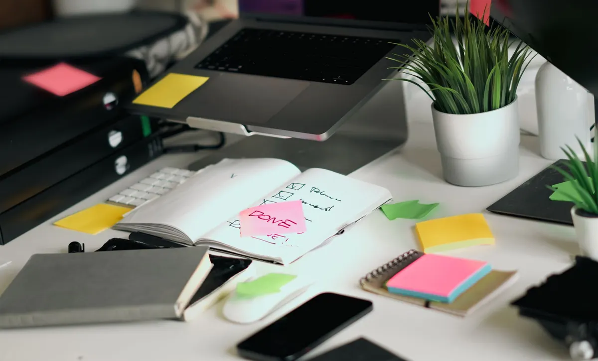 A handwritten checklist in an open notebook beside a laptop on a wooden desk.