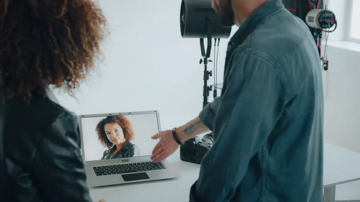 A photographer and a client look at a laptop together at a café table while they plan a shoot.