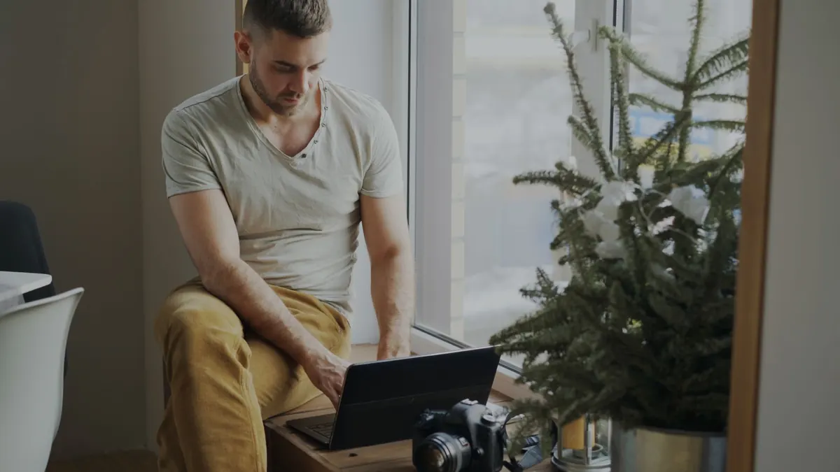 A freelance designer checks an invoice on a laptop at a home desk beside a notebook and a cup of coffee.