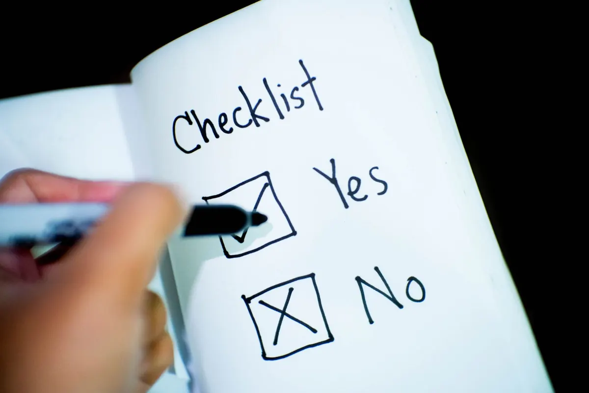 A person ticking items off a handwritten checklist in a notebook next to a keyboard.