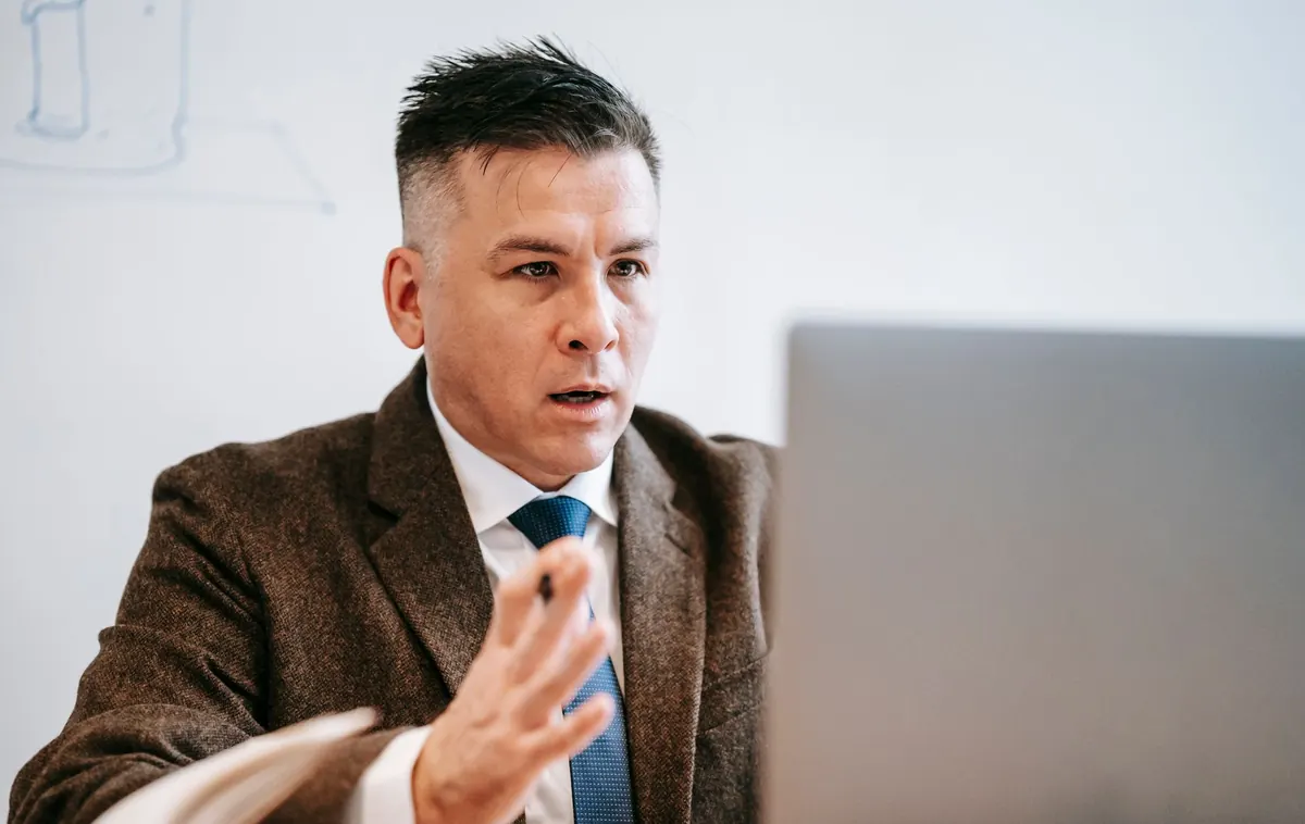 An account manager on a video call with a client, taking notes at a desk beside a laptop.