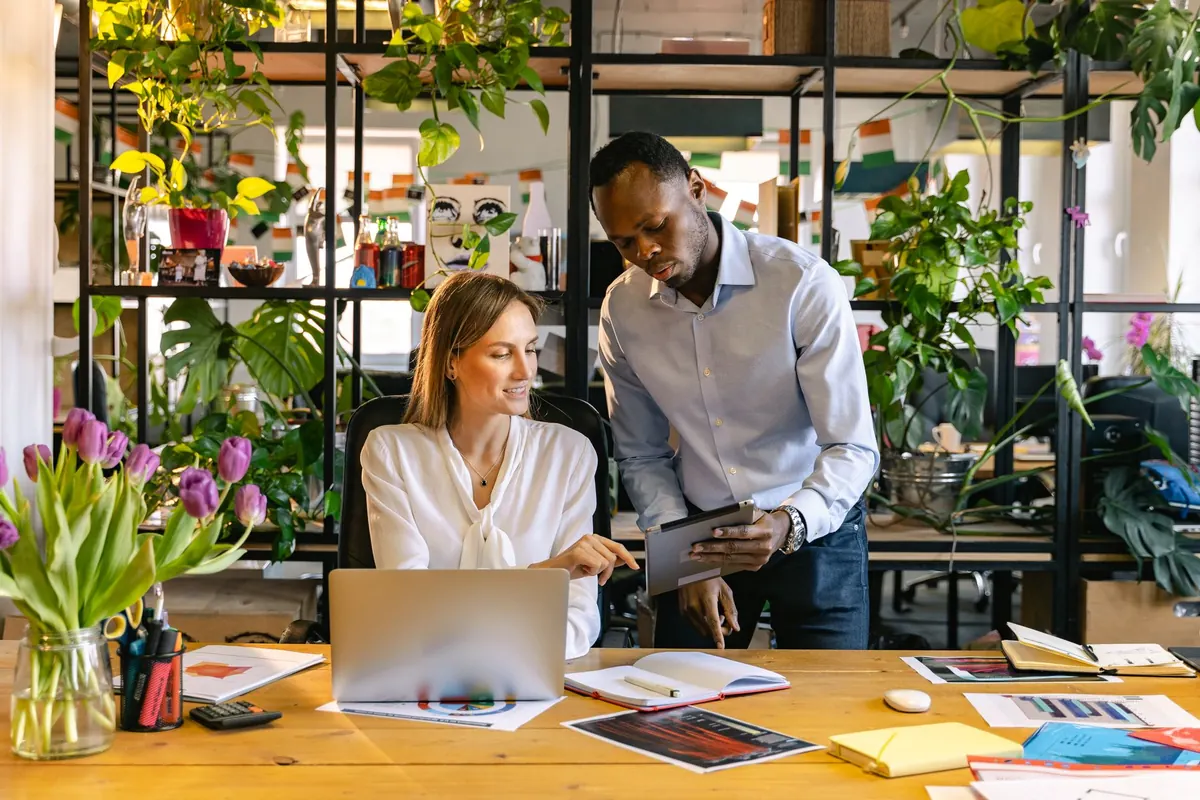 Three colleagues look at customer records together on a laptop in a small office.