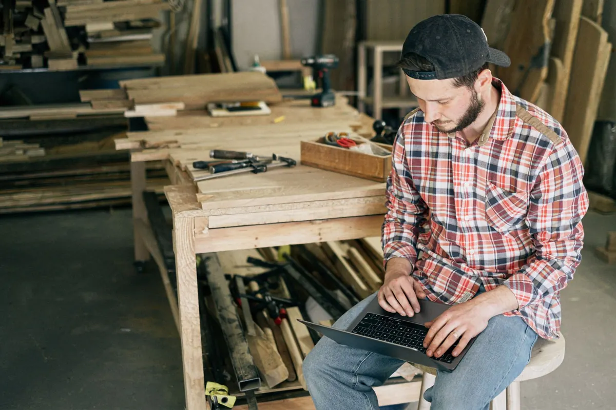 A small business owner at a laptop in a craft studio, working on the product pages of their online shop.