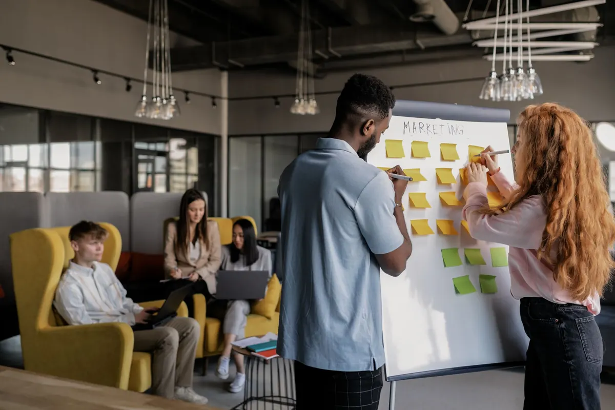 Three colleagues in a small office plan their customer follow-up on a whiteboard.