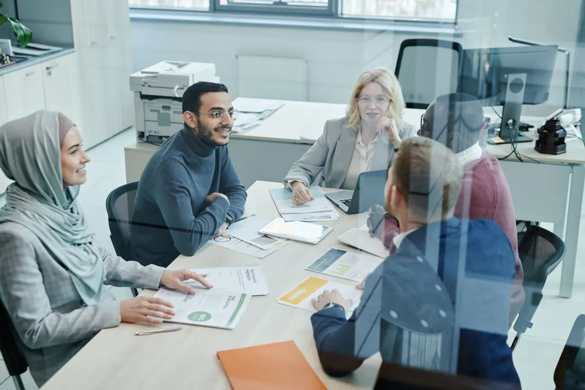 A small sales team talks through deals around a table with laptops in a bright office.