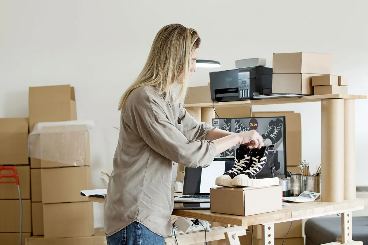 A small online shop owner packing customer orders into cardboard boxes at a workbench.
