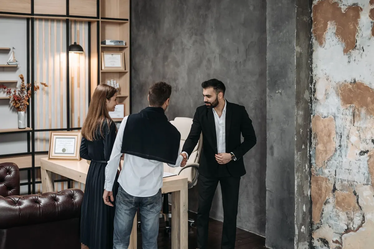 A web designer shows a website layout on a laptop to a small business owner across a desk.