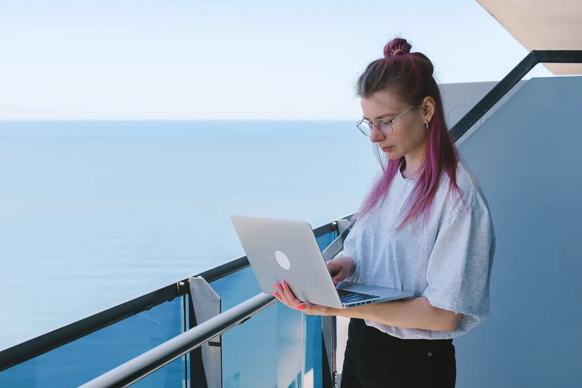A freelancer at a desk compares monthly software costs on a laptop beside a notebook and calculator.
