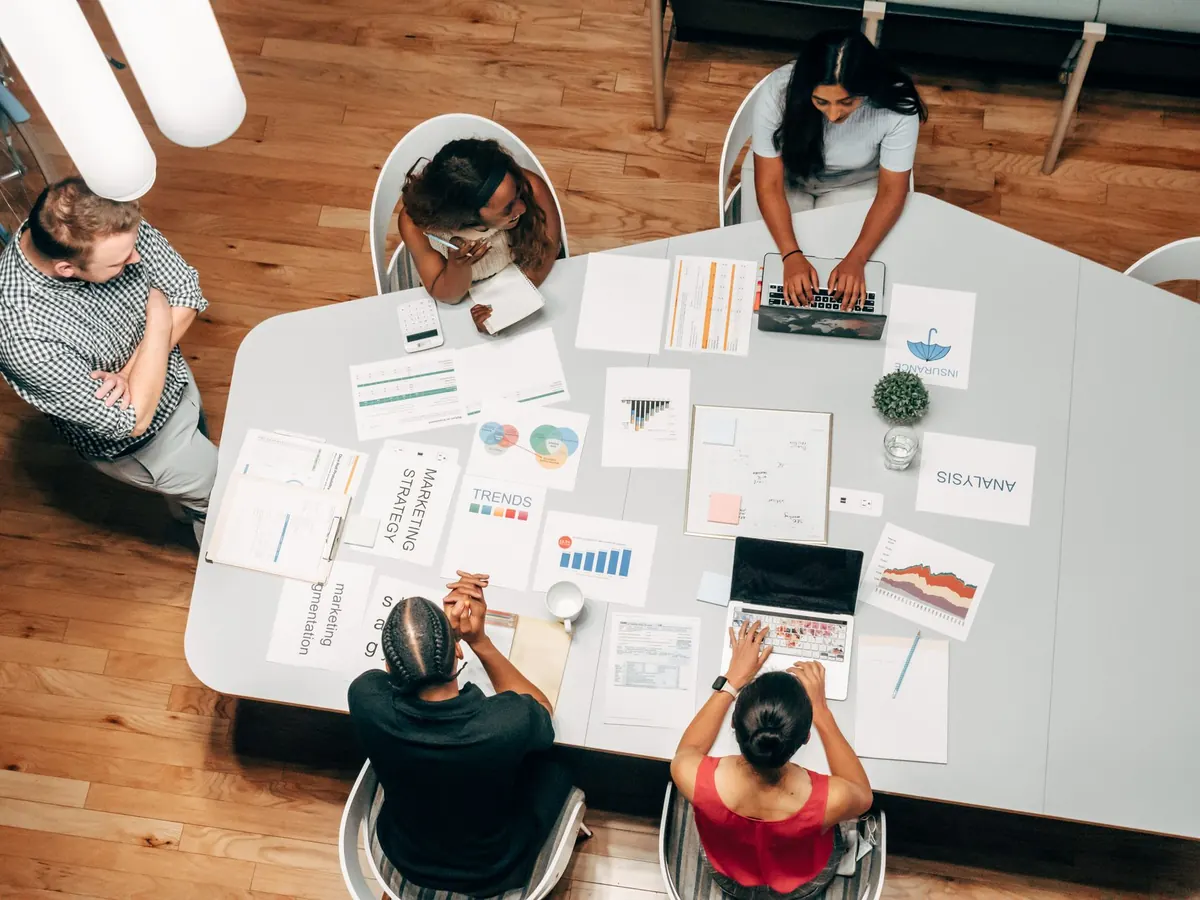 A small agency team talks through client work around a table with laptops and notes.