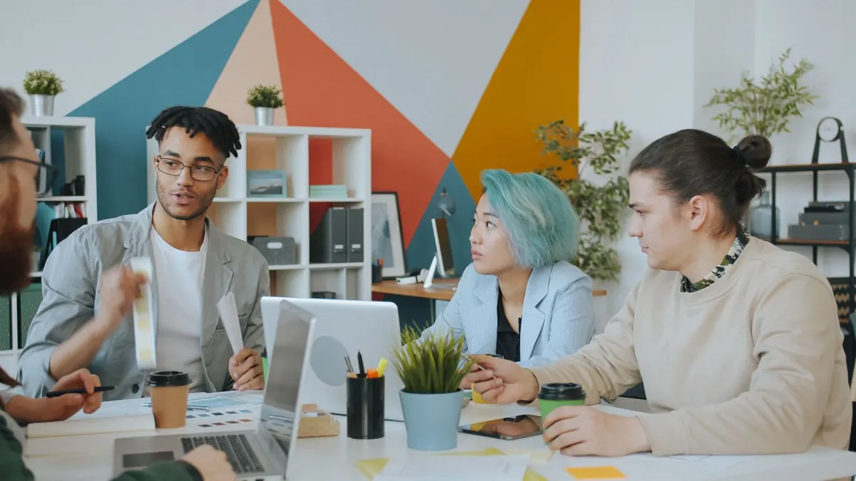 Three colleagues gathered around a laptop in a small agency office, talking through a client project.