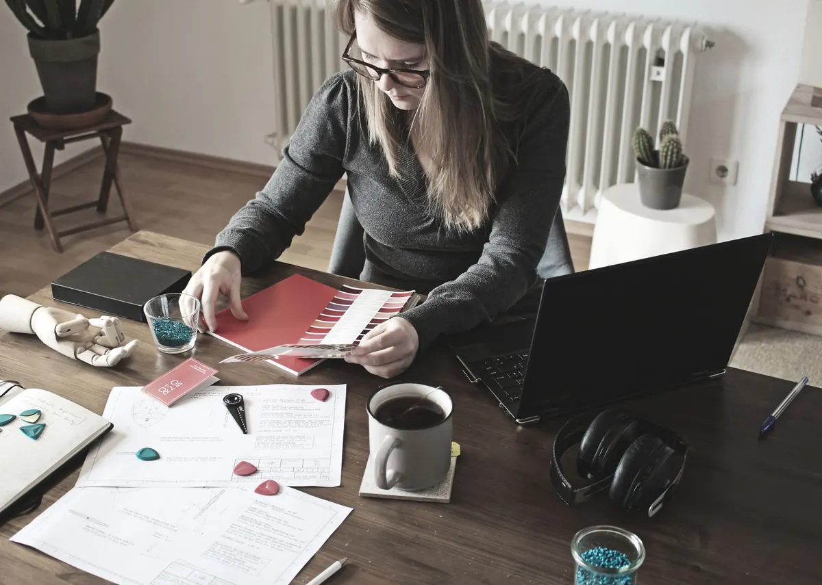 A freelance web designer at a desk reviewing a pricing document on a laptop screen.
