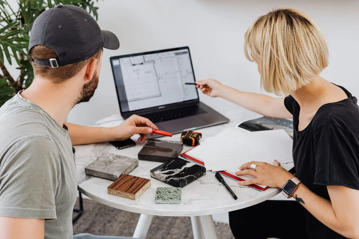 Two people at a small table discussing notes and figures on a laptop during a client meeting.