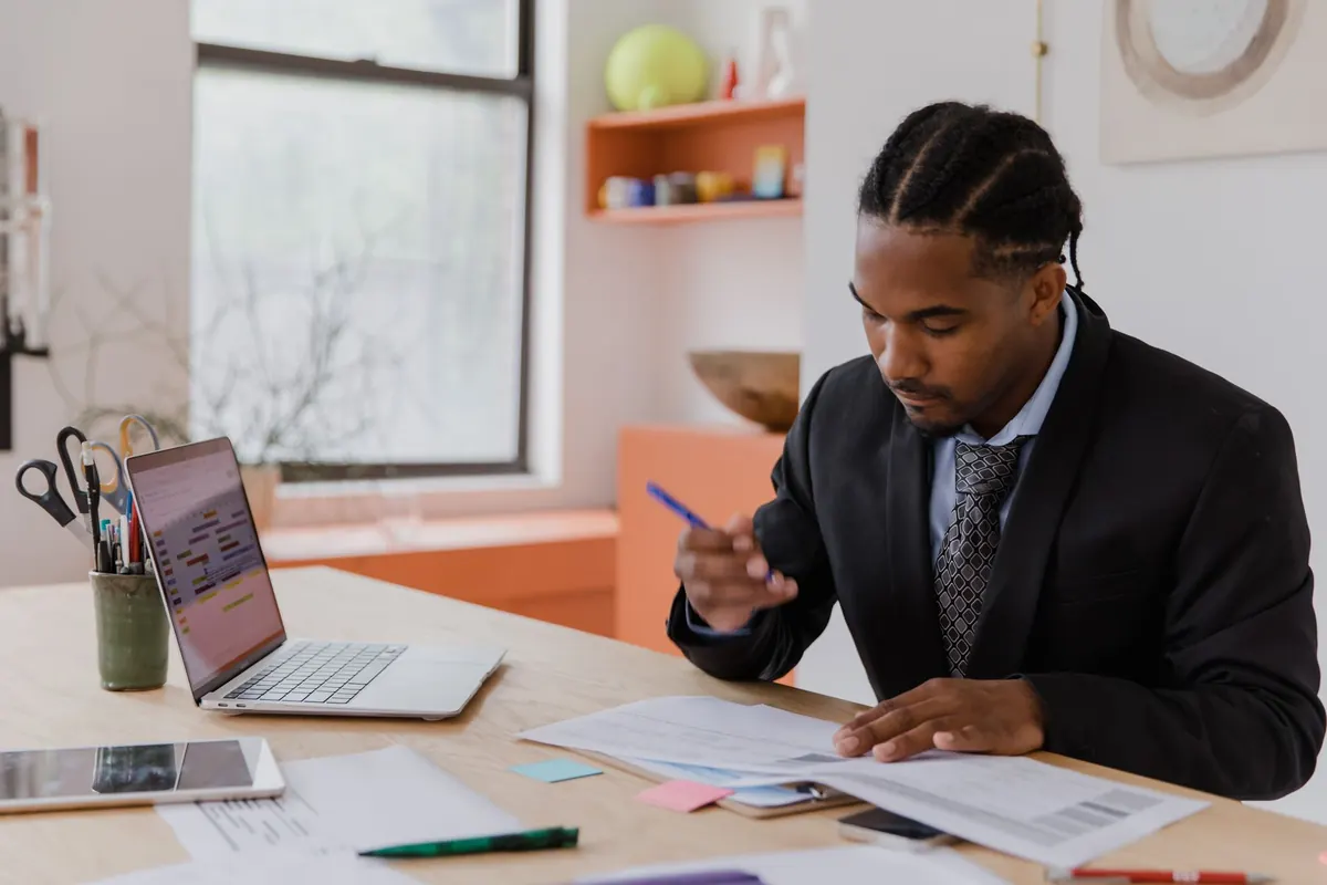 An agency owner checks monthly client invoices on a laptop at a desk with a notebook and coffee.
