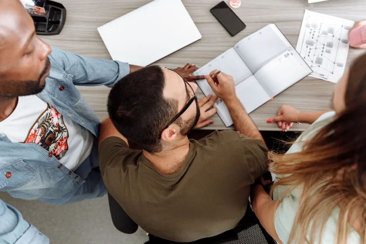 A small product team talks through plans around a table with laptops in a bright office.