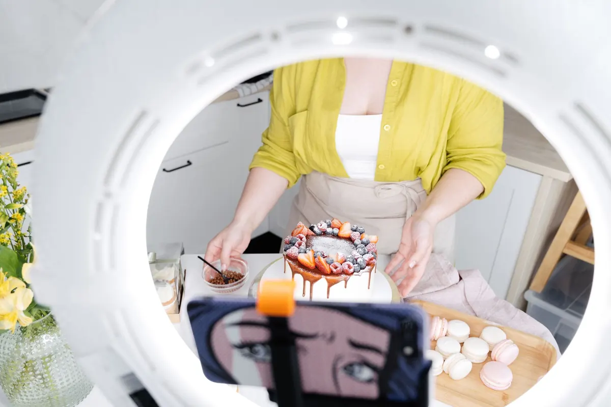A baker uses a phone to photograph a tray of fresh cakes for their website.