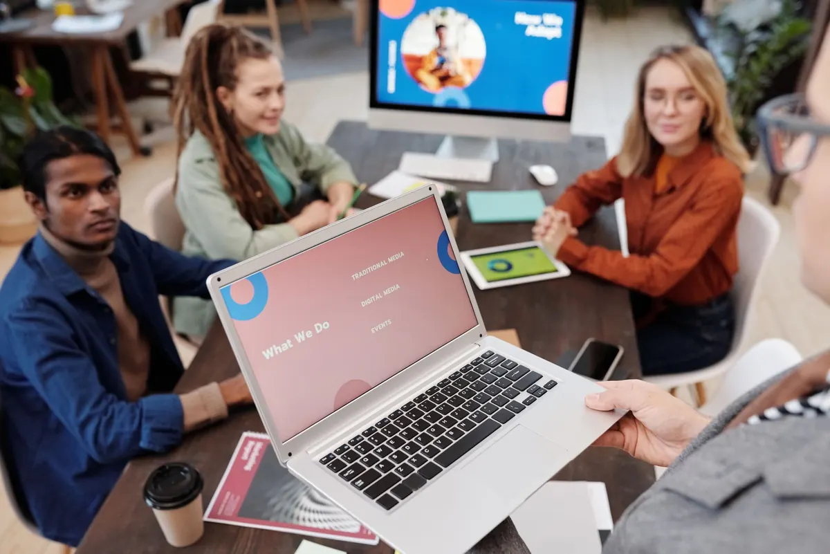 A small web design team discusses a client website around a laptop in a bright office.